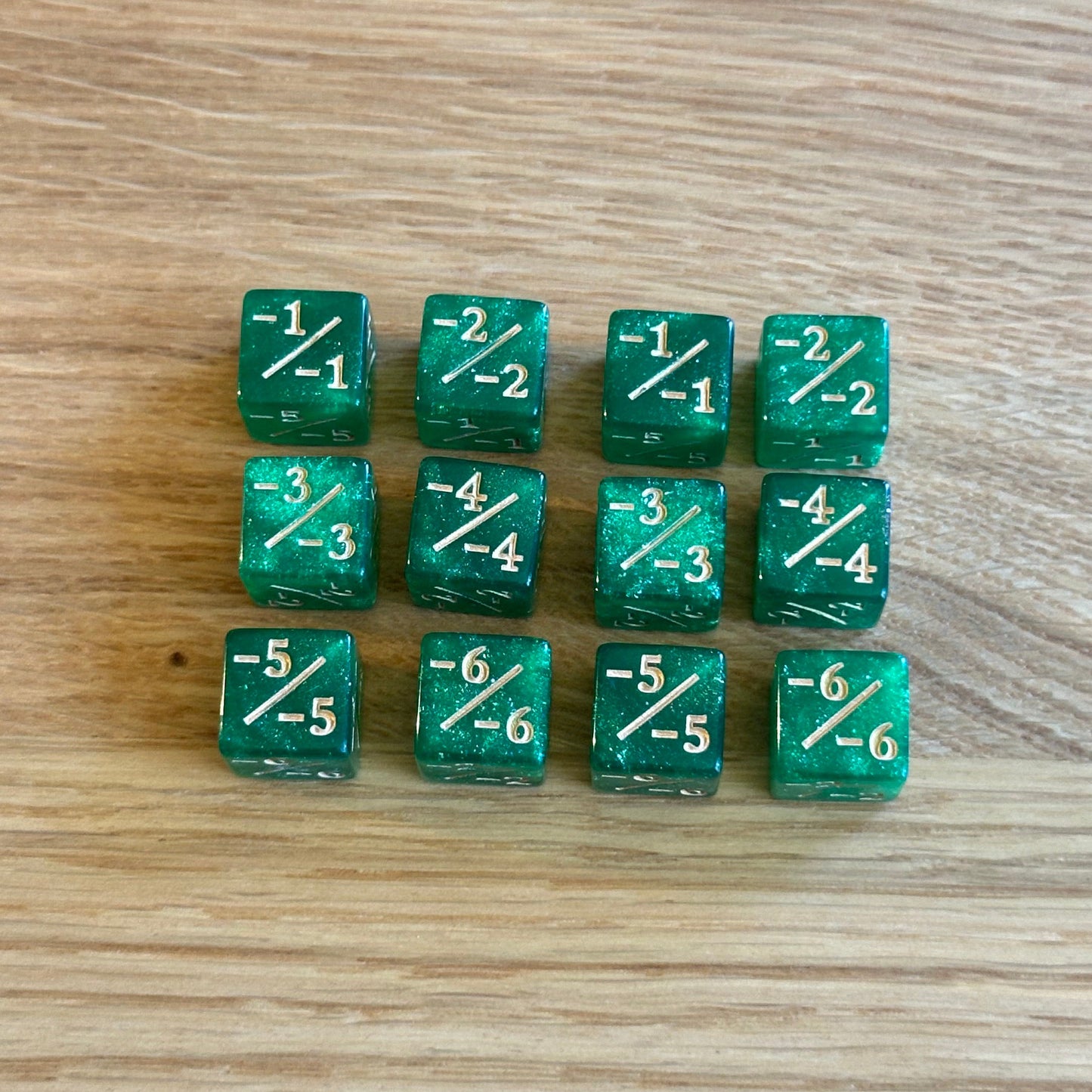Set of twelve 12mm D6 -/- minus minus dice in glitter green with gold infill. each dice is numbered 1-6 on each side to track incremental negative modifiers.