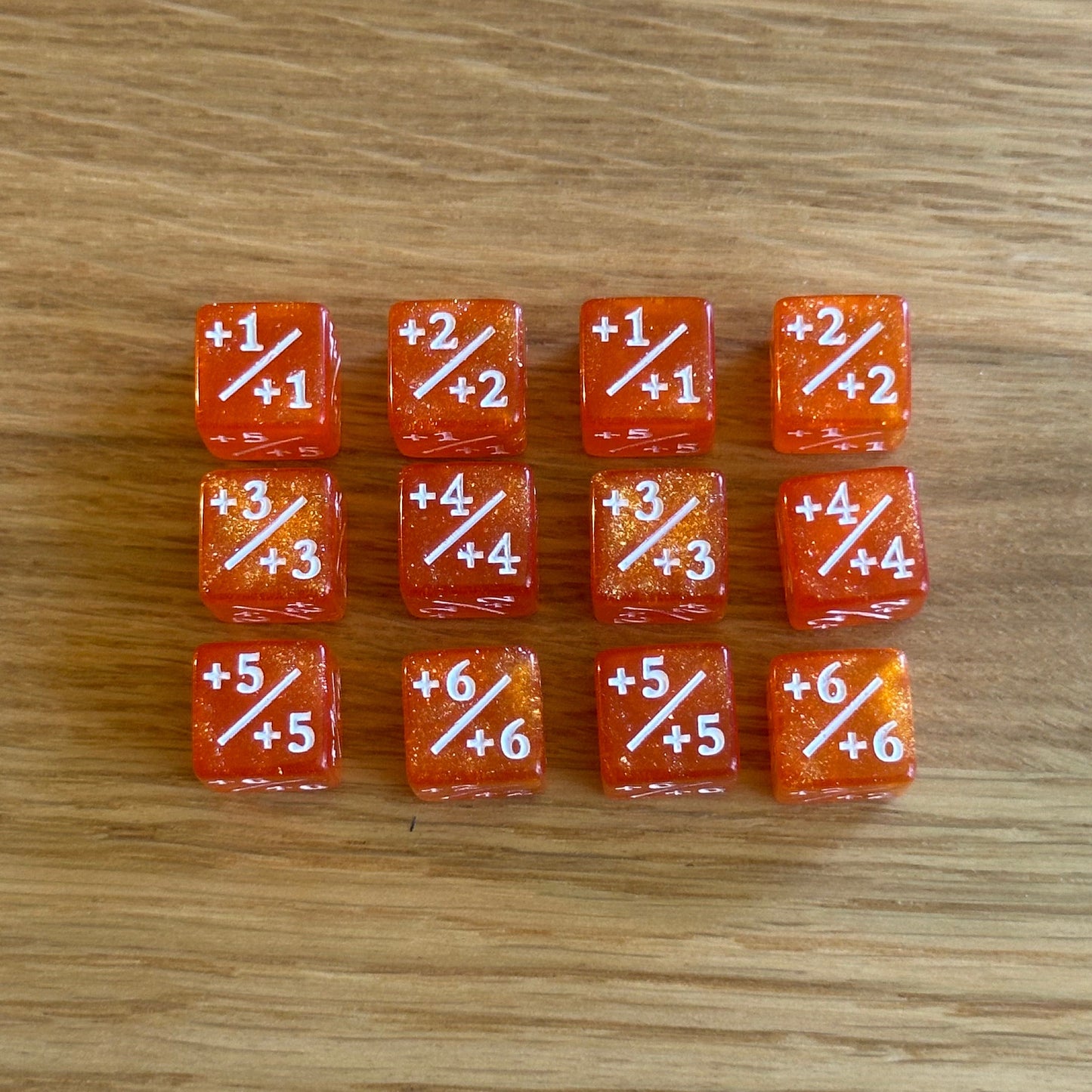 Set of twelve 12mm D6 +/+ plus plus dice in glitter orange with white infill. each dice is numbered 1-6 on each side to track incremental positive modifiers.