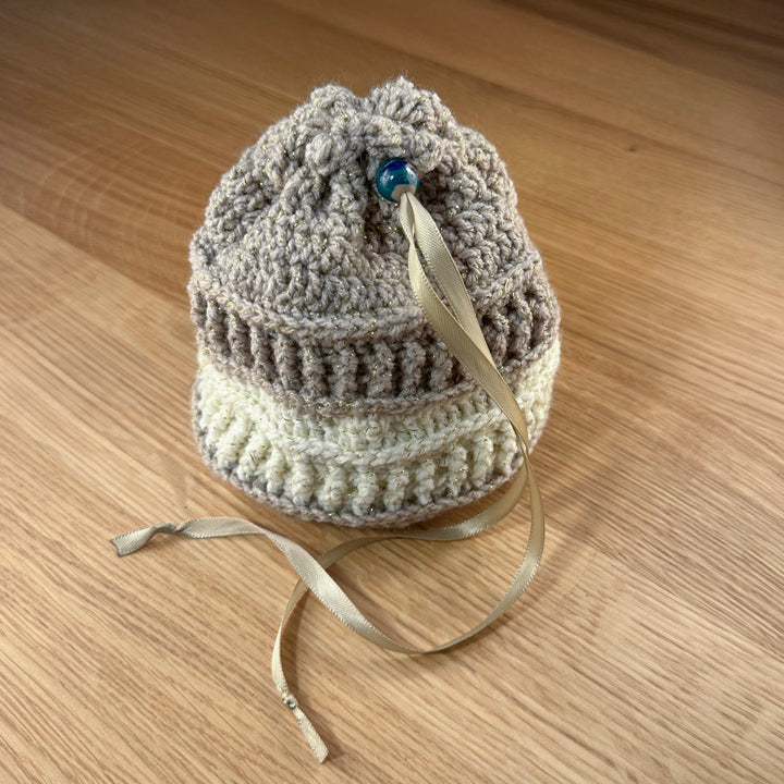 Closed tan and cream crochet dice bag with a teal glass bead closure. Part of the handmade hoard and fateweaver's collection.